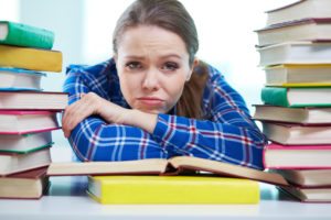 Portrait of a frustrated student being surrounded with piles of books