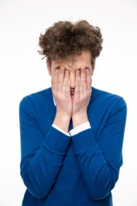 Man with curly hair covers his face with hands